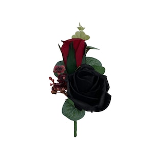 May include: A floral boutonniere with a black rose and a red rose, complemented by green leaves and small burgundy buds. The arrangement is set against a white background, highlighting the contrasting colours.