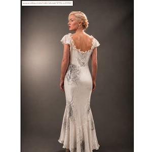 May include: A floor-length cream-colored dress with short ruffled sleeves and a scoop neckline. The fabric features a dark gray abstract print with swirling patterns. The garment has a fitted bodice and a flared hemline, showing a back view.