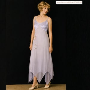 Puede incluir: Un vestido lencero de color lavanda con tirantes finos, escote en V y bajo asimétrico. El vestido presenta un delicado bordado floral en el lateral e incluye el texto www.etsy.com/uk/shop/STILLCHIC en la esquina superior derecha.