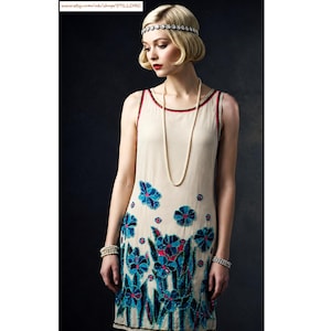 May include: A sleeveless cream-colored shift dress featuring a vibrant floral pattern in shades of blue, teal, and magenta. The garment is adorned with a long pearl necklace, a beaded headband, and two beaded bracelets on the wrists.