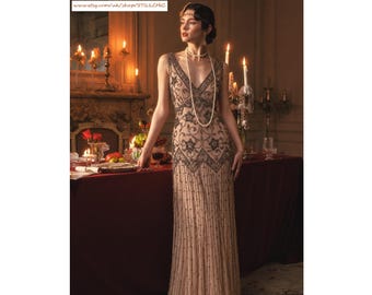 May include: A floor-length sleeveless gown in a light beige hue, featuring a deep V-neckline and intricate black beadwork arranged in star and scroll patterns. The dress is adorned with vertical beaded lines and a long white pearl necklace.