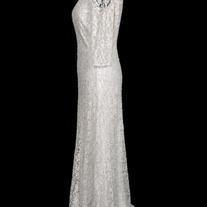 Puede incluir: Un vestido blanco largo con una delicada capa de encaje. El vestido presenta mangas largas y un escote en V sutil. Los detalles de encaje se extienden a las mangas y al dobladillo, creando un look rom&aacute;ntico y elegante. El vestido se muestra en un maniqu&iacute; negro.