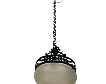 Könnte beinhalten: Schwarze Schmiedeeisen-Pendelleuchte mit einem matten Glasschirm. Die Leuchte hat eine dekorative Kette und ein detailliertes Metalldesign.