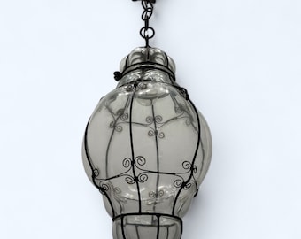 May include: A clear glass pendant light fixture with a black metal cage. The cage has a decorative scroll design.