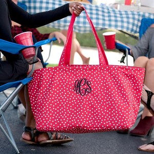 May include: A red and white polka dot tote bag with a black monogram. The bag has two handles and is large enough to carry many items.