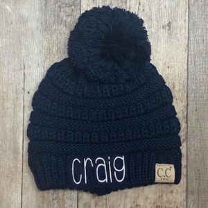May include: Black knit beanie with a pom pom on top and the name "craig" embroidered on the front. The beanie has a small brown tag with the text "CC Kids" on it.