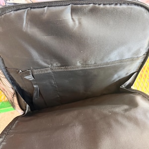 Puede incluir: Mochila negra con un estampado de cerdos. El interior es negro con m&uacute;ltiples compartimentos. El exterior presenta cerdos rosas con un dise&ntilde;o de valla de madera. La mochila tiene una cremallera negra y un bolsillo lateral de malla.