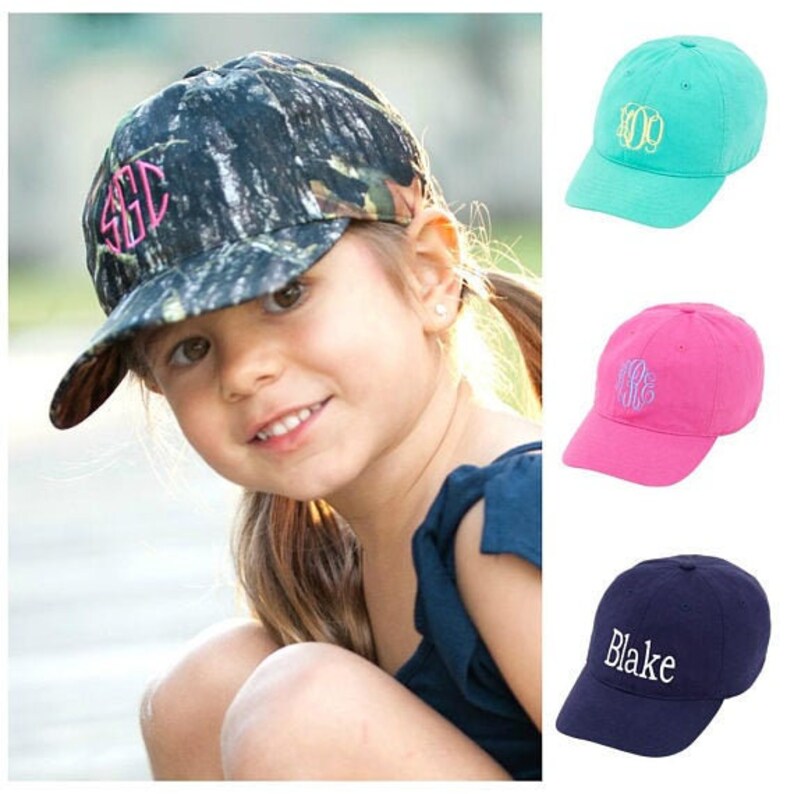 May include: Three different styles of baseball caps with embroidered initials. The caps are in camouflage, teal and pink.