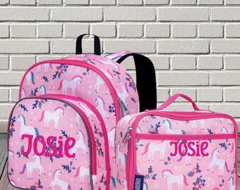 May include: A pink backpack and a matching lunch bag, both featuring a repeating pattern of white unicorns and colorful flowers. Each item is personalized with the name Josie embroidered in bold pink script on the front pocket.