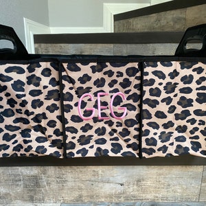 May include: A black fabric storage bin with three compartments. The bin has a leopard print pattern and the initials "GEG" are embroidered on the front in pink.