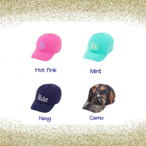 May include: Four baseball caps in different colours and patterns. The caps are arranged in a grid. The top left cap is hot pink with a monogram, the top right cap is mint green with a monogram, the bottom left cap is navy blue with the name "Blake" embroidered on it, and the bottom right cap is camo with a brown and green pattern.