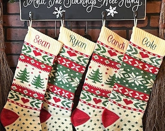 May include: Four Christmas stockings with personalized names: Sean, Ryan, Candi, and Cole. The stockings have a cream-colored base with red and green patterns, including trees, hearts, and snowflakes. The stocking toes are red, and the cuffs are cream-colored.