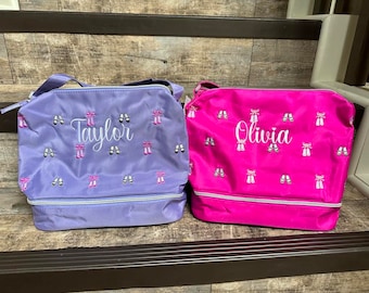 May include: Two personalized dance bags, one purple with the name "Taylor" and one pink with the name "Olivia" embroidered on them. Both bags feature a pattern of ballet shoes with pink bows.