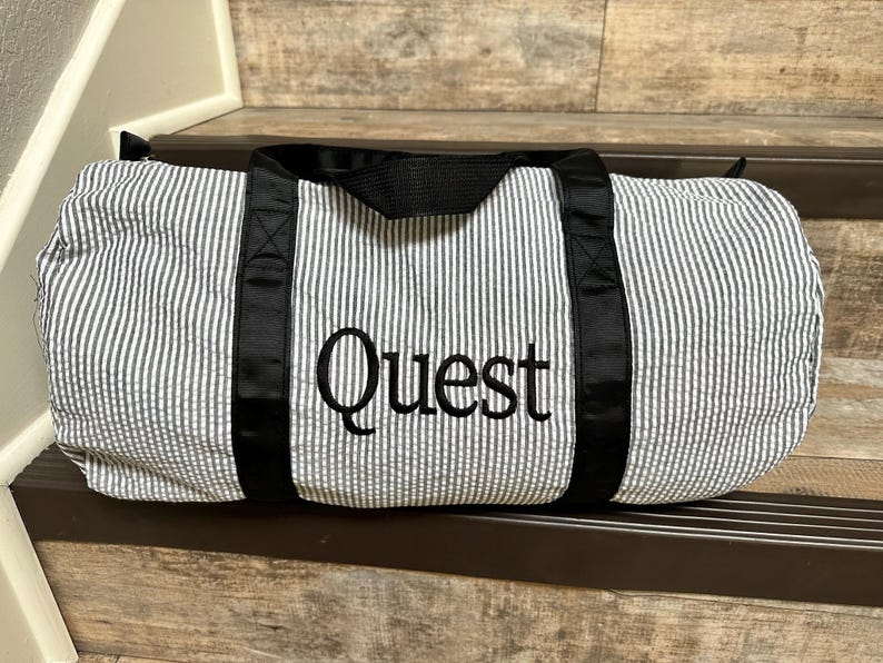 May include: A black and white striped duffel bag with black straps and the word "Quest" embroidered in black on the front.