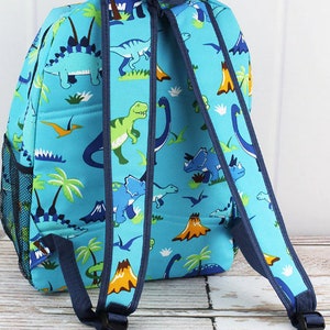 May include: A blue backpack with a dinosaur print. The backpack has two adjustable straps and a mesh pocket on the side.