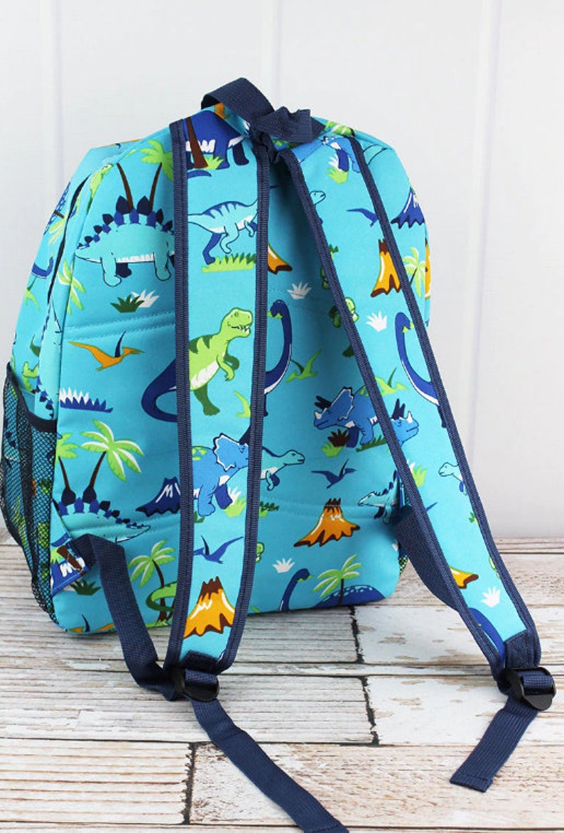 May include: A blue backpack with a dinosaur print. The backpack has two adjustable straps and a mesh pocket on the side.