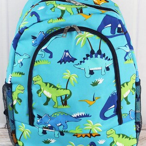 May include: A blue backpack featuring a dinosaur print. The backpack has a large main compartment with a zipper closure, two side pockets, and a mesh pocket on the front. The dinosaurs are green, blue, and orange.