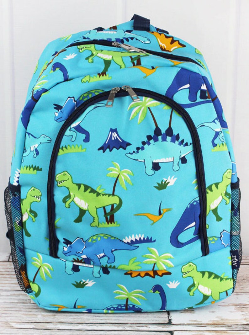 May include: A blue backpack featuring a dinosaur print. The backpack has a large main compartment with a zipper closure, two side pockets, and a mesh pocket on the front. The dinosaurs are green, blue, and orange.