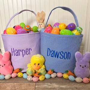 May include: Two Easter baskets filled with colorful plastic eggs. The purple basket is labeled "Harper" and the blue basket is labeled "Dawson".  A pink bunny, a yellow duck, and a purple bunny are in front of the baskets.
