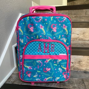 May include: A teal blue and pink rolling suitcase with a mermaid pattern and the monogram "AMR" on the front.