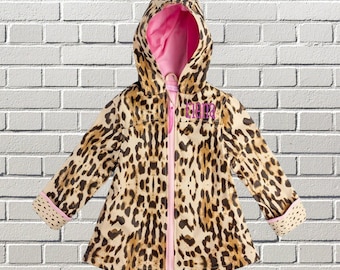 May include: A hooded raincoat featuring a tan and black leopard print pattern. The jacket has a bright pink interior lining, a full-length pink front zipper, and the name Elena embroidered in pink thread on the upper left chest area.