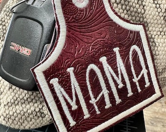 Könnte beinhalten: Burgunderfarbener Leder-Schlüsselanhänger mit einer weißen Stickerei "MAMA".