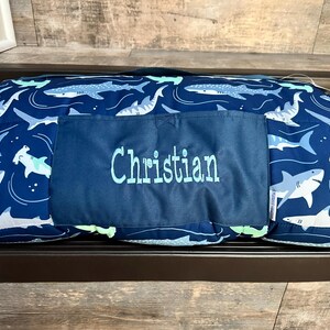 May include: A blue and white shark-themed sleeping bag with a personalized pocket that says "Christian".