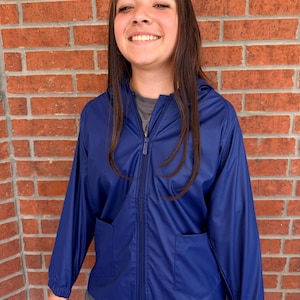 May include: A navy blue hooded jacket with a full-length zipper and two front pockets. The jacket is made of a smooth, shiny material. The person is wearing a gray t-shirt underneath.