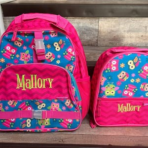 May include: Two pink backpacks with owl designs. The larger backpack has a zippered front pocket and a mesh side pocket. The smaller backpack has a zippered front pocket. Both backpacks have the name "Mallory" embroidered on the front.