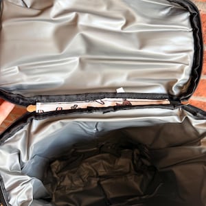 Puede incluir: Bolsa de almuerzo aislante negra abierta con interior plateado. La bolsa tiene una cremallera negra y un ribete estampado. El interior es de un material plateado reflectante, dise&ntilde;ado para mantener el contenido fr&iacute;o o caliente. La bolsa est&aacute; abierta, revelando el espacioso interior.