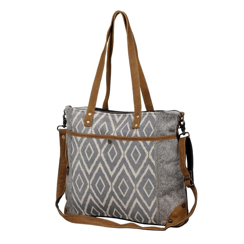 May include: A gray and white geometric patterned tote bag with brown leather straps and accents. The bag has a top zipper closure and a detachable shoulder strap.