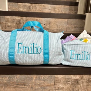 May include: Two blue and white striped travel bags with turquoise handles and the name "Emilio" embroidered on them.