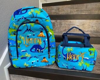 May include: A blue and green dinosaur-themed backpack and lunch bag set with the name "Henry" embroidered on both.