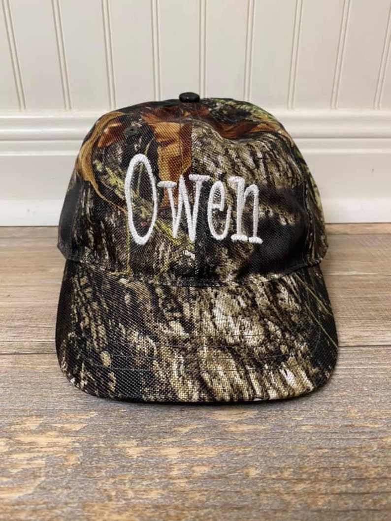 May include: A camouflage baseball cap with the name "Owen" embroidered in white on the front.