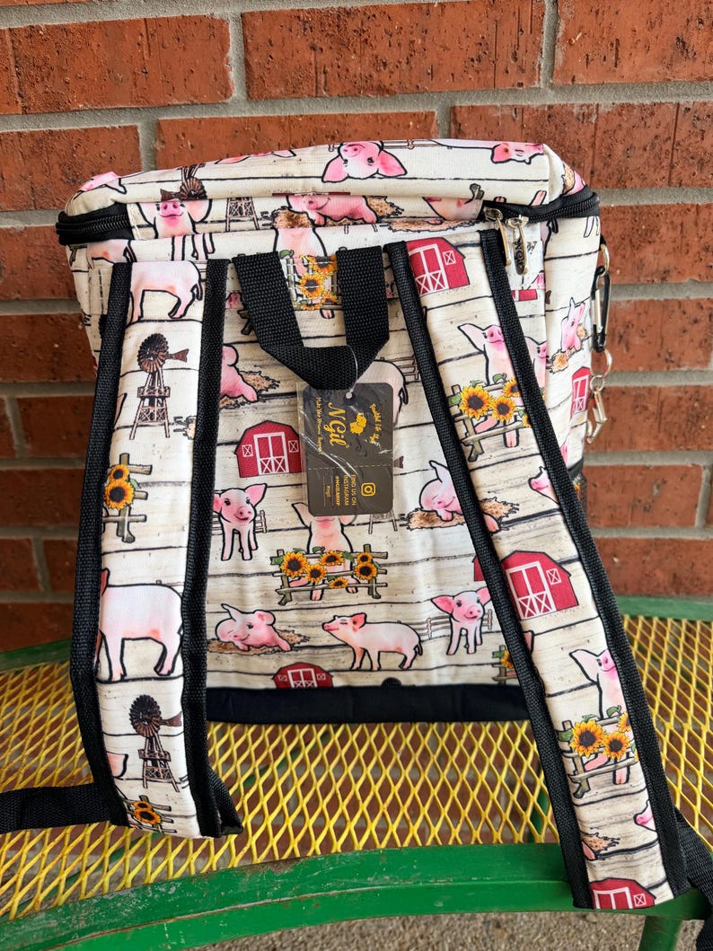Puede incluir: Mochila con tem&aacute;tica de animales de granja. La mochila presenta un estampado de cerdos rosas, graneros rojos, girasoles y molinos de viento sobre un fondo blanco. Tiene correas negras y una cremallera negra.