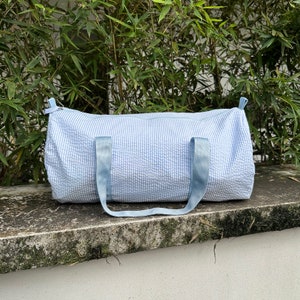 May include: A light blue duffel bag with white stripes. The bag has two blue straps and a zipper closure.