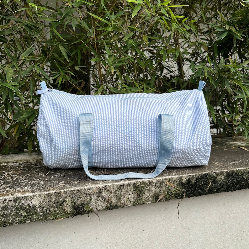 May include: A light blue duffel bag with white stripes. The bag has two blue straps and a zipper closure.