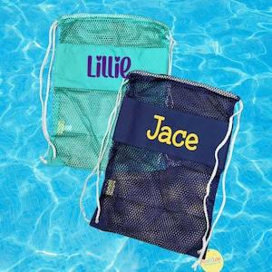 May include: Two drawstring backpacks made of mesh and solid fabric. One is teal with the purple name Lillie, and the other is navy blue with the yellow name Jace. Both bags feature white rope straps and a rectangular center panel for personalization.