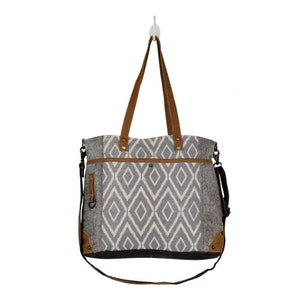 May include: A gray and white tote bag with a geometric pattern. The bag has brown leather handles and a brown leather strap. The bag has a zippered pocket on the front.