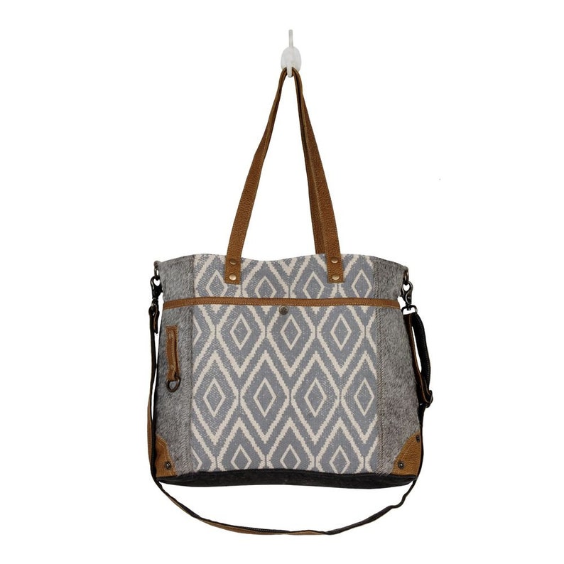 May include: A gray and white tote bag with a geometric pattern. The bag has brown leather handles and a brown leather strap. The bag has a zippered pocket on the front.