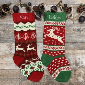 May include: Two knitted Christmas stockings, one red and one green, with festive patterns and the names "Mary" and "Kathleen" embroidered on them. The stockings feature reindeer, trees, and geometric designs.