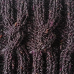 May include: Close-up of a dark gray knitted fabric with a textured pattern. The fabric has a subtle sheen and a slightly rough texture.