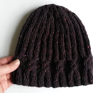 May include: A dark brown knitted beanie with a cable knit pattern and flecks of pink throughout.