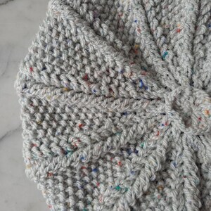 K&ouml;nnte beinhalten: Nahaufnahme eines grauen gestrickten Stoffes mit bunten Flecken. Der Stoff ist strukturiert und hat ein gewebtes Muster.
