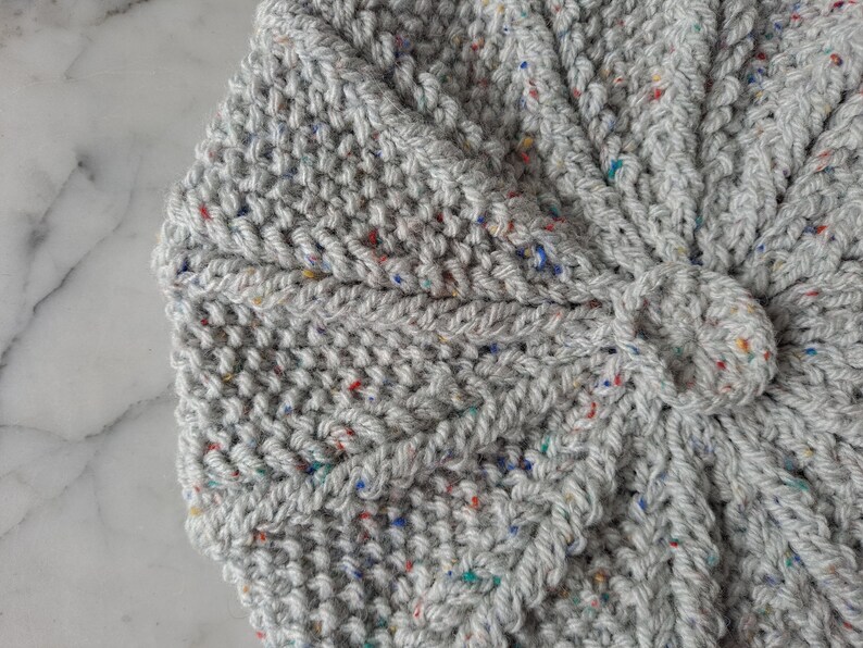 K&ouml;nnte beinhalten: Nahaufnahme eines grauen gestrickten Stoffes mit bunten Flecken. Der Stoff ist strukturiert und hat ein gewebtes Muster.
