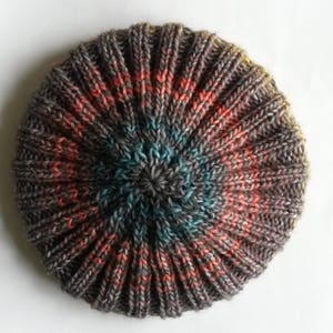 May include: A hand-knitted beanie with a colorful striped pattern in shades of gray, pink, blue, and yellow. The beanie is made with a textured stitch that gives it a unique look.