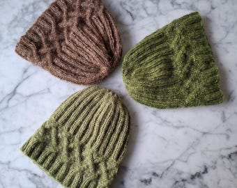 May include: Three knitted hats, one brown and two green, with a cable knit pattern. The hats are arranged on a white marble surface.