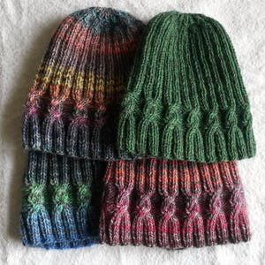 May include: Three knitted hats in different colors and patterns. The top hat is green, the middle hat is a rainbow ombre, and the bottom hat is a dark red ombre.