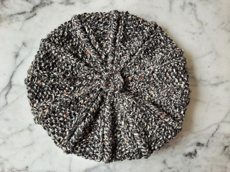 K&ouml;nnte beinhalten: Eine schwarze und wei&szlig;e Strickm&uuml;tze mit einem strukturierten Muster. Die M&uuml;tze ist aus einem weichen, warmen Material gefertigt und hat einen klassischen Stil.