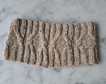 May include: A beige knitted headband with a cable knit pattern.